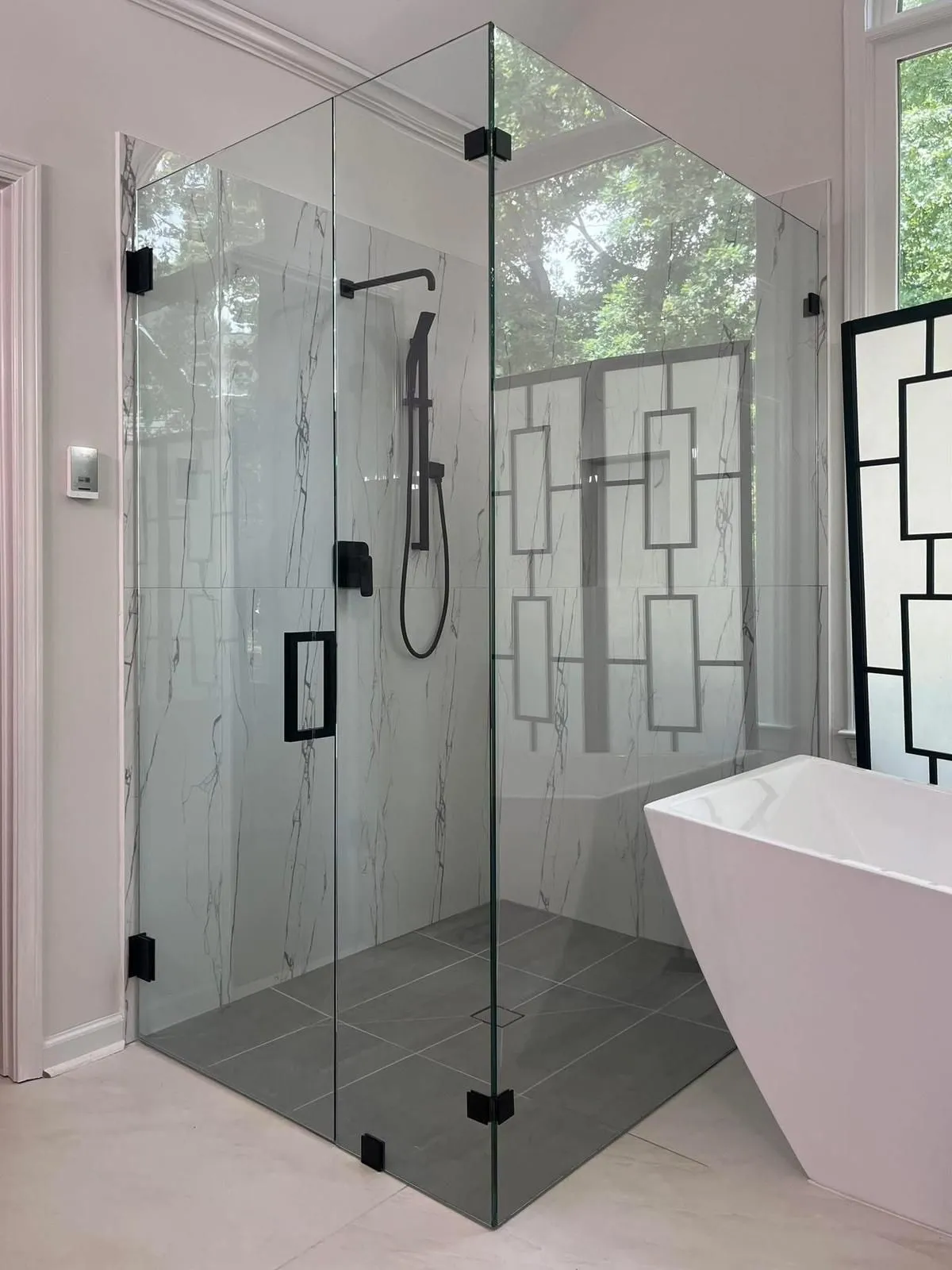 Glass shower enclosure with black hardware, marble-look tile, and modern shower fixtures in a bathroom.