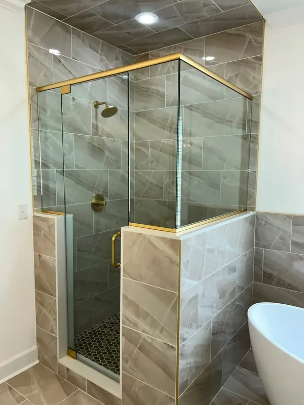 Frameless 90-degree glass shower enclosure on a tiled knee wall with gold brass hardware