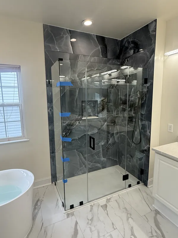 Frameless shower door installation with matte black hinges and handle